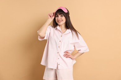 Photo of Happy woman in pyjama and sleep mask on beige background