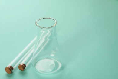 Photo of Flask and test tubes on turquoise background, space for text. Laboratory glassware