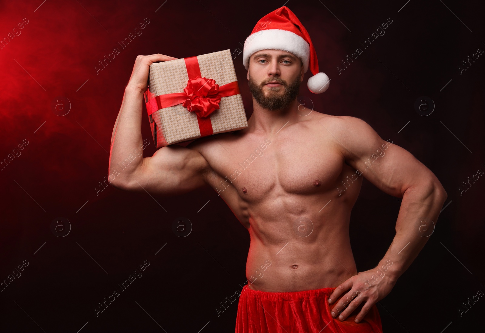 Photo of Attractive young man with muscular body holding Christmas gift box on color background