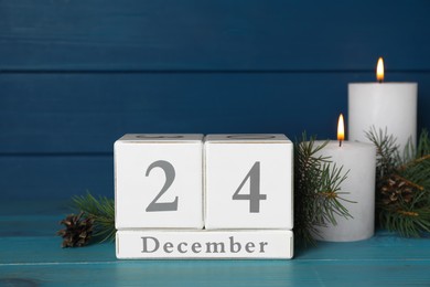 Photo of Christmas Eve - December 24. Block calendar, burning candles and fir tree branches on light blue wooden table