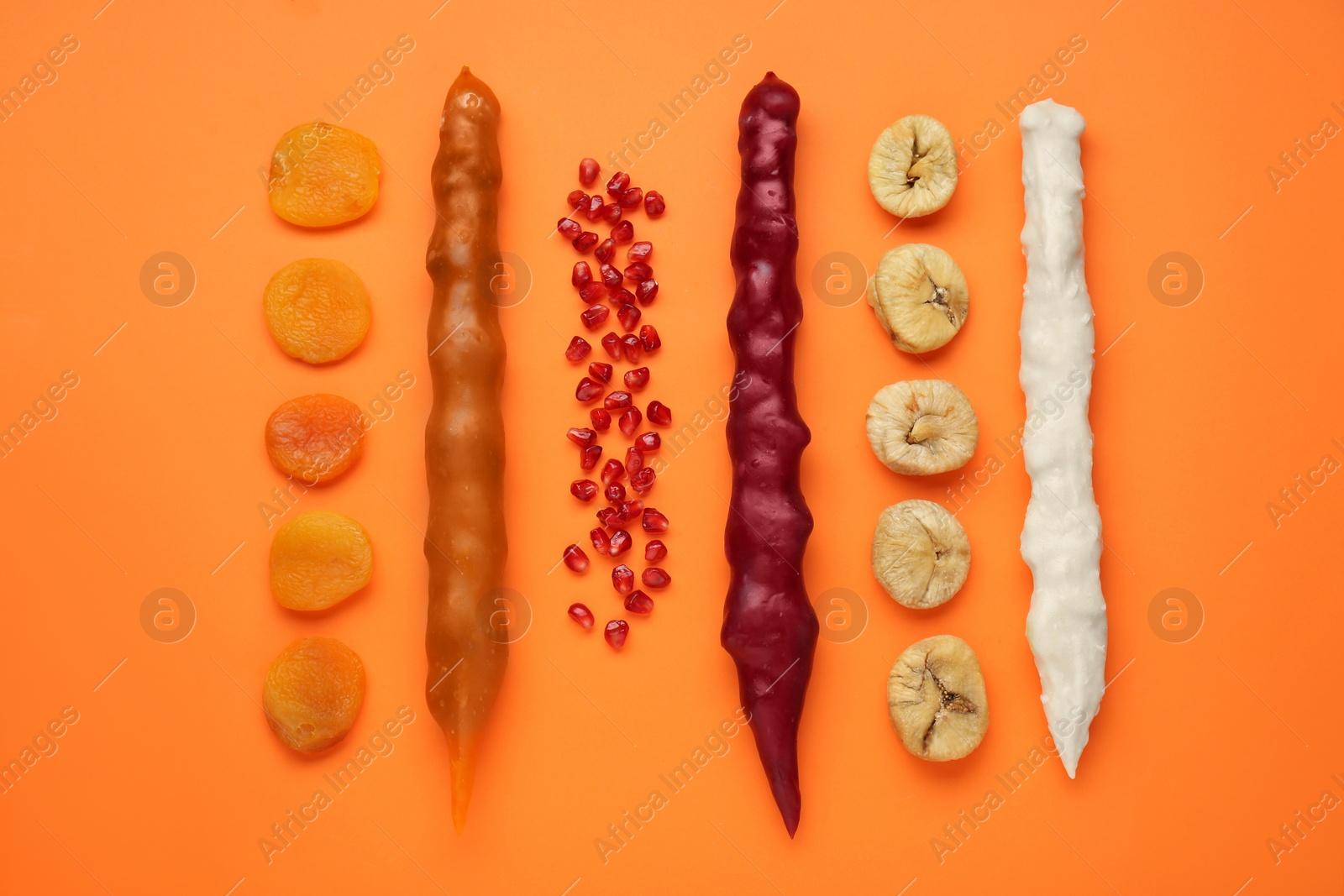 Photo of Delicious churchkhelas and fruits on orange background, flat lay