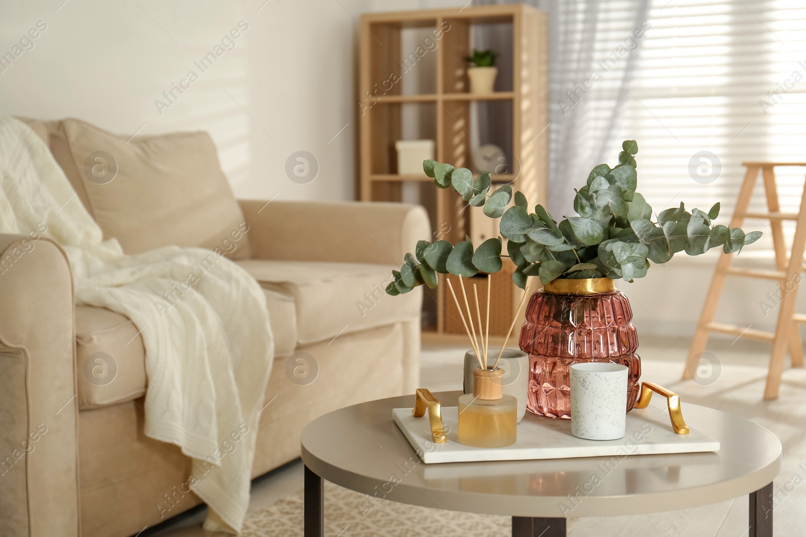 Photo of Bunch of eucalyptus branches and oil diffuser on table in living room. Interior design