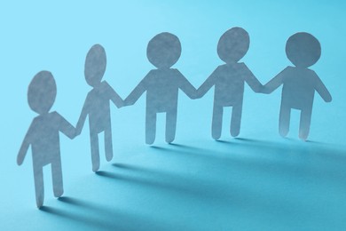 Photo of Teamwork concept. Paper figures of people holding hands on light blue background