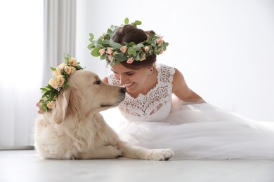 Bride and adorable Golden Retriever wearing wreath made of beautiful flowers indoors