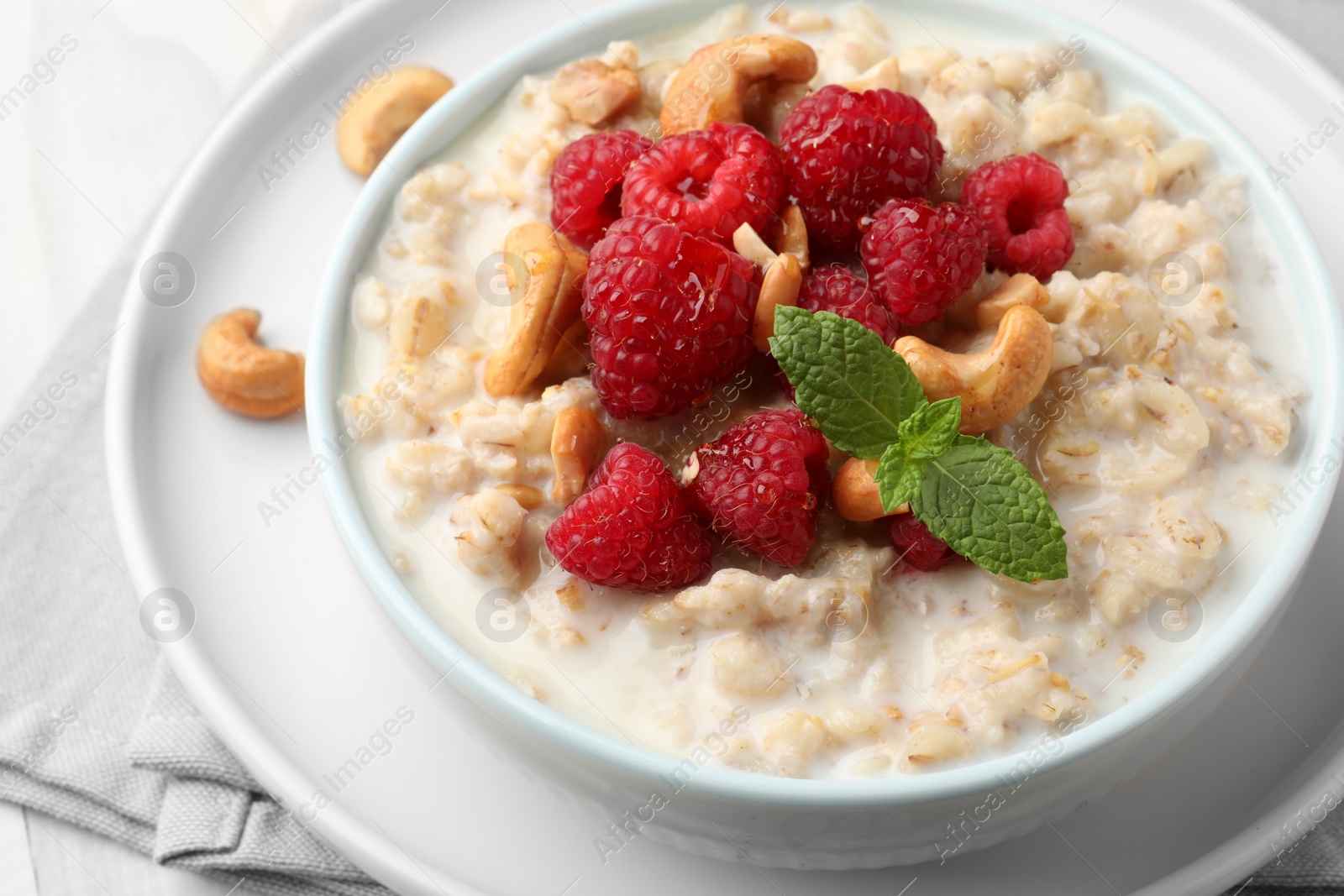 Photo of Bowl with tasty oatmeal porridge with nuts and raspberries on table, closeup. Healthy meal