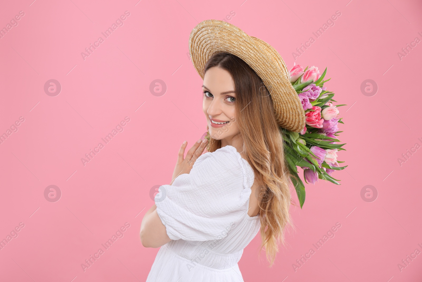 Photo of Happy young woman in straw hat holding bouquet of beautiful tulips on pink background