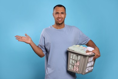 Young man with basket full of laundry on light blue background