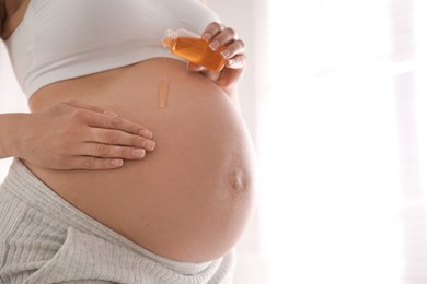 Photo of Young pregnant woman with cosmetic product indoors, closeup. Space for text