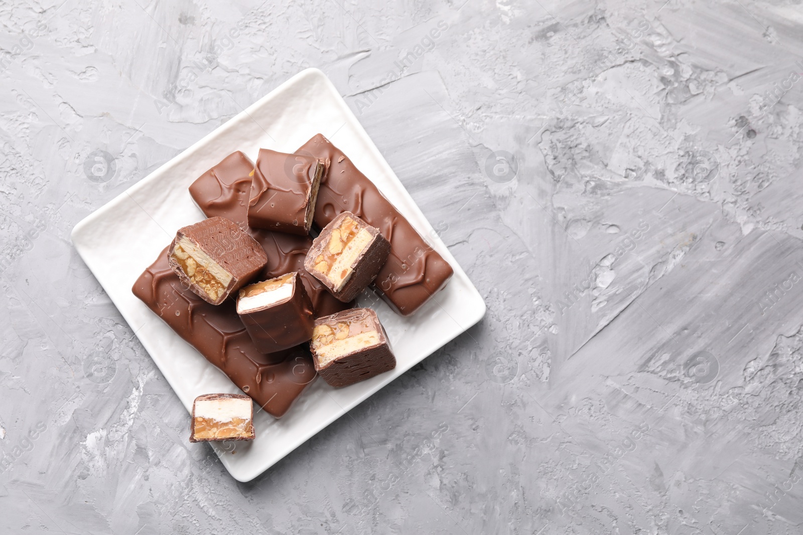 Photo of Tasty chocolate bars with nougat on gray textured table, top view. Space for text