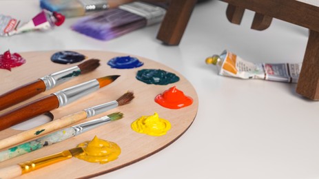 Photo of Artist's palette with samples of colorful paints and brushes on white table. Space for text