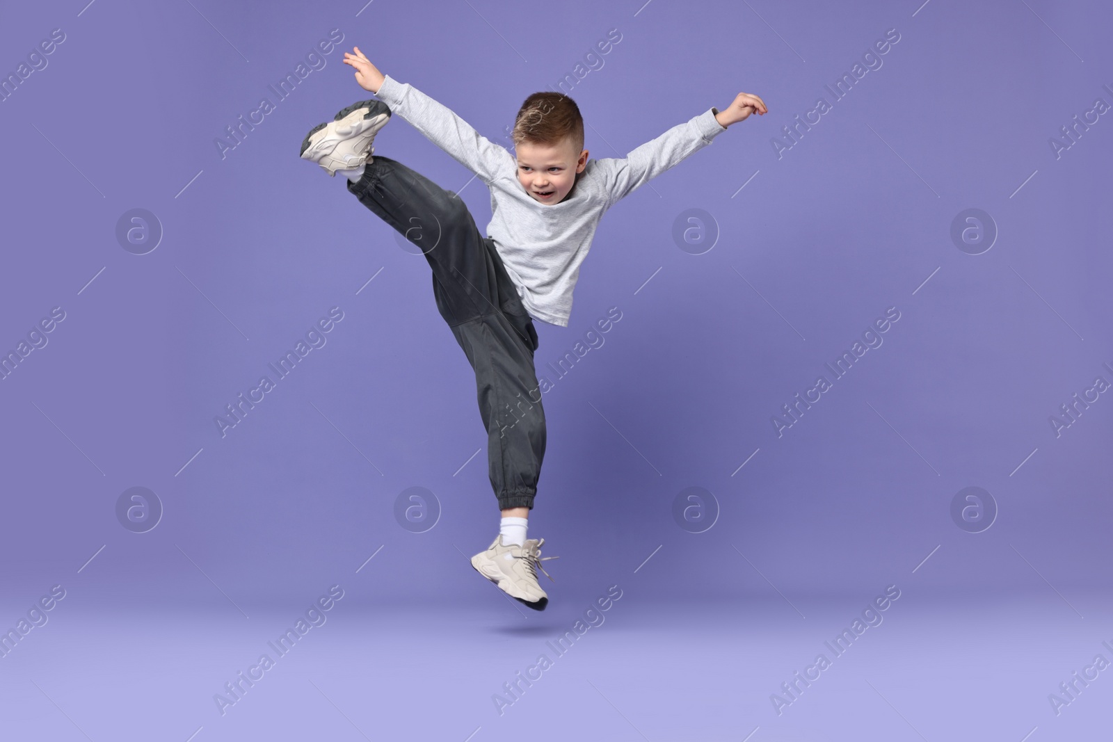 Photo of Happy little boy dancing on violet background. Space for text