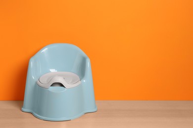 Photo of Light blue baby potty on wooden table against orange background, space for text. Toilet training