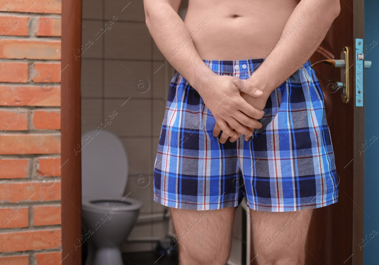 Photo of Young man with urological problems suffering from pain near toilet