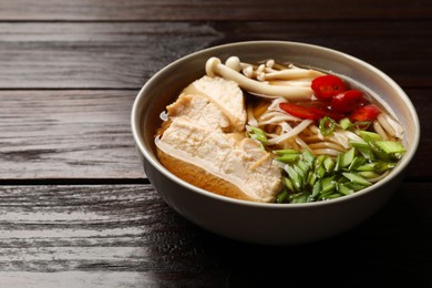 Delicious ramen with meat and mushrooms in bowl on wooden table, closeup. Space for text