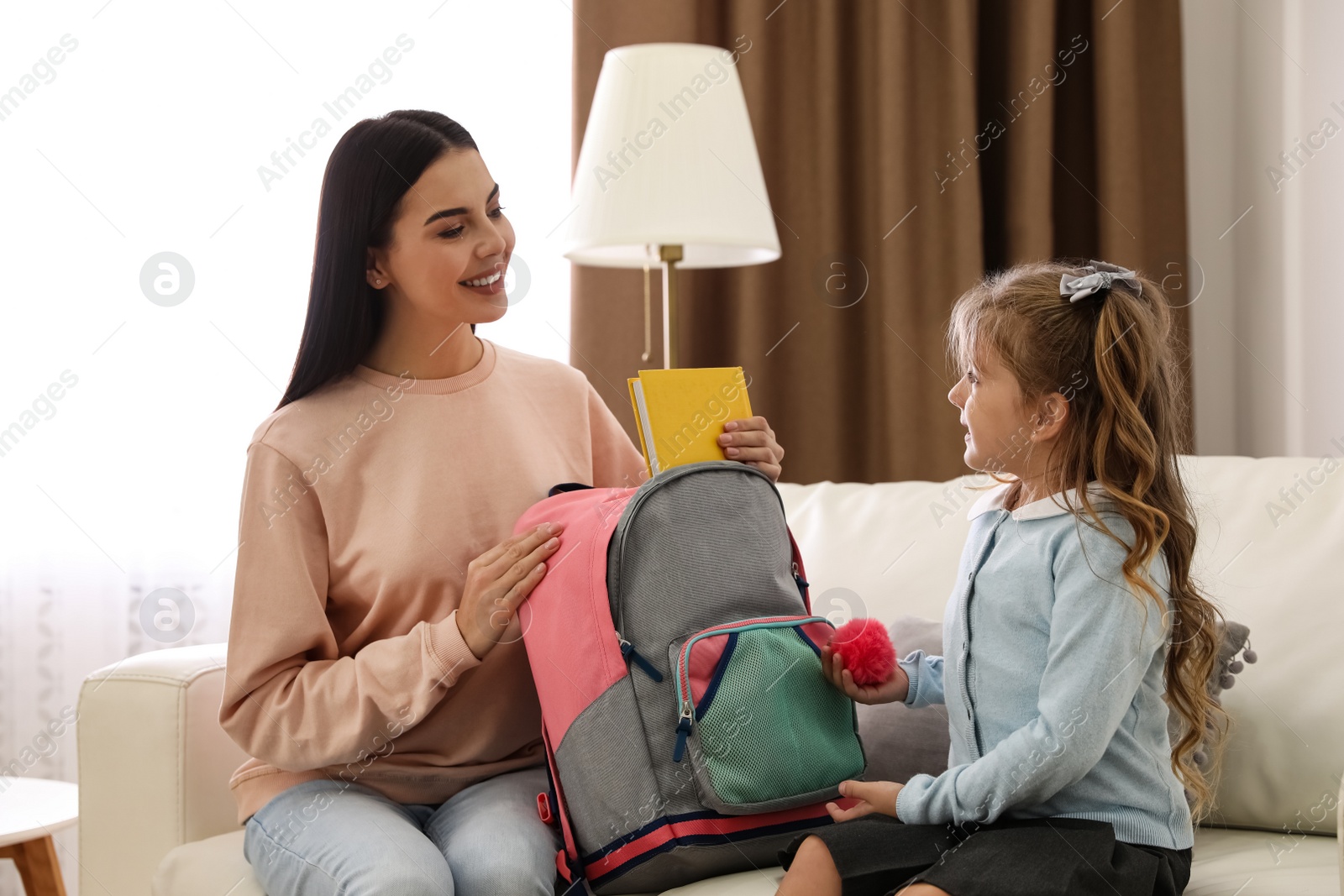 Photo of Young mother helping her little child get ready for school at home