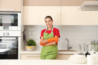 Photo of Beautiful young woman wearing gloves and apron in clean kitchen. Dish washing