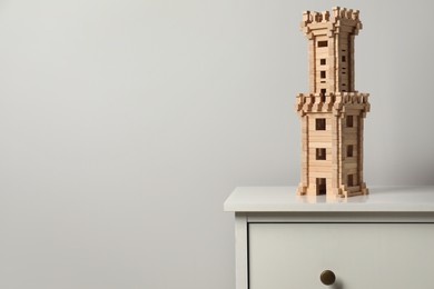 Photo of Wooden tower on chest of drawers near light grey wall, space for text. Children's toy