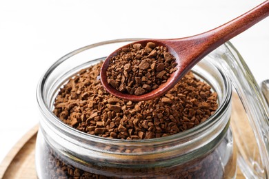 Spoon of instant coffee over jar on white table, closeup