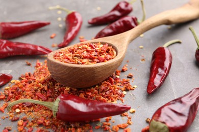 Photo of Chili pepper flakes, pods and spoon on grey table, closeup