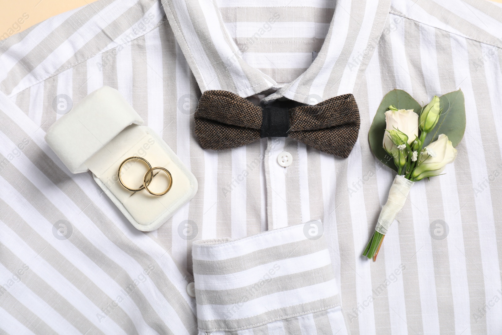Photo of Wedding stuff. Stylish boutonniere, shirt, bow tie and rings, top view