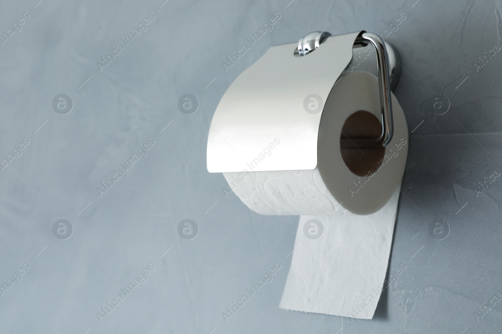 Photo of Holder with toilet paper roll on gray background. Space for text