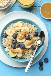 Photo of Tasty oatmeal with banana, blueberries and peanut butter served in bowl on light blue wooden table, flat lay