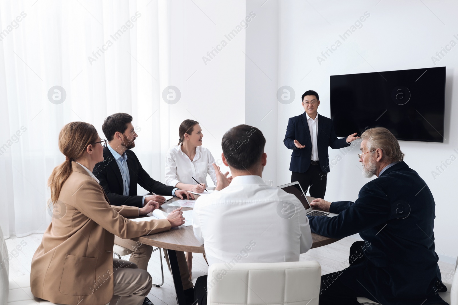 Photo of Business conference. Group of people listening to speaker report near tv screen in meeting room