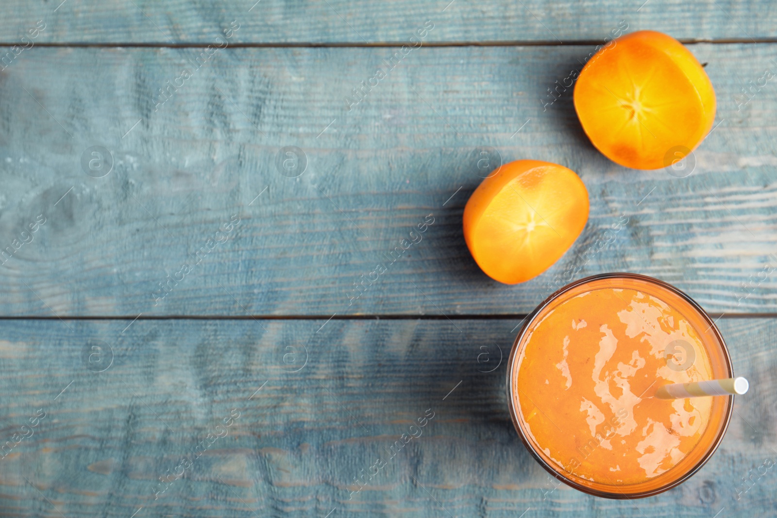 Photo of Tasty persimmon smoothie with straw and fresh fruits on light blue wooden table, flat lay. Space for text