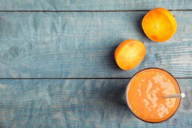 Tasty persimmon smoothie with straw and fresh fruits on light blue wooden table, flat lay. Space for text