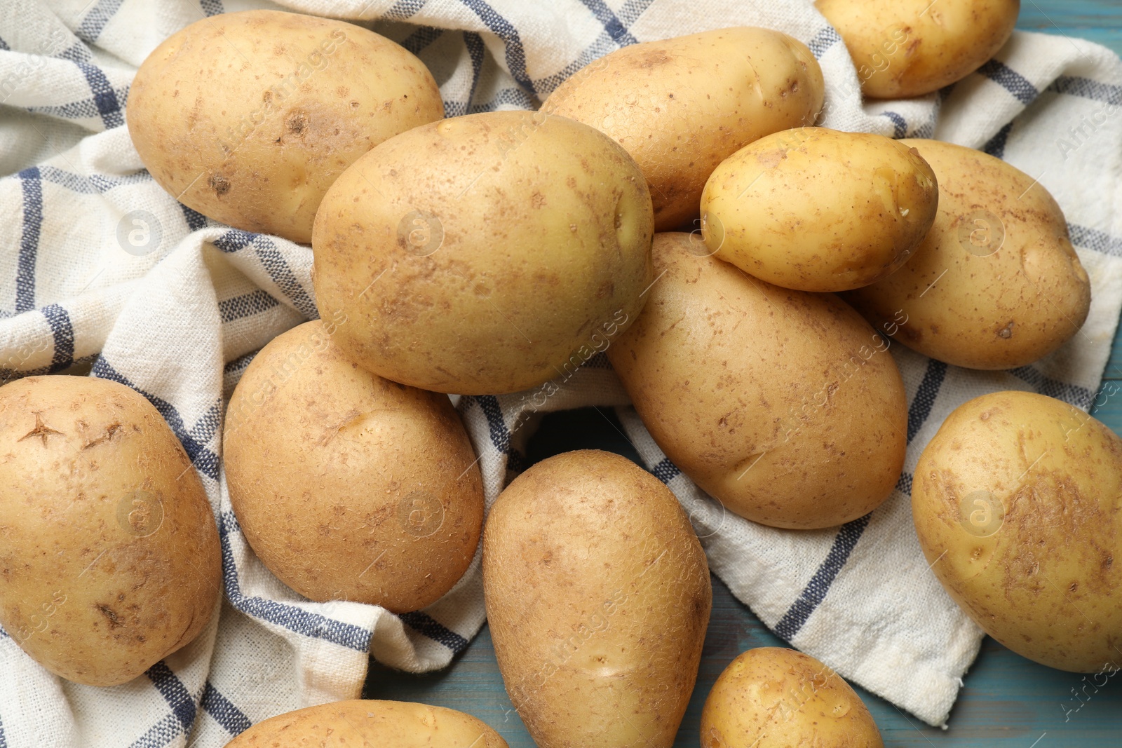 Photo of Raw fresh potatoes and napkin on light blue wooden table