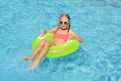 Photo of Cute little girl with inflatable ring in pool on sunny day