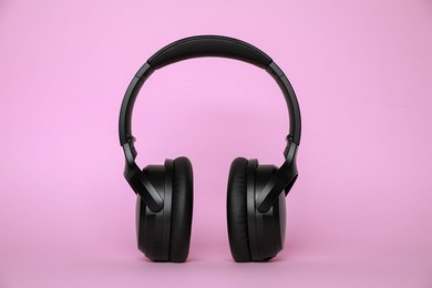 Photo of Modern black wireless headphones on pink background