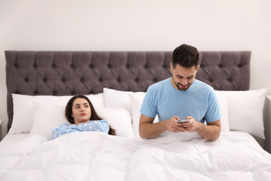 Photo of Young man preferring smartphone over his girlfriend in bed at home