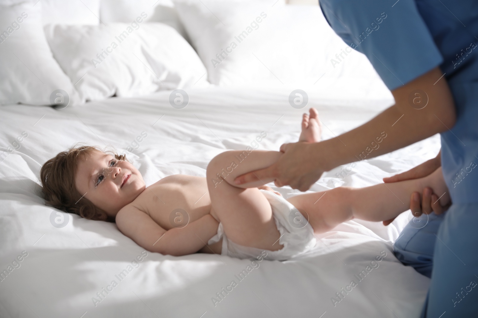 Photo of Orthopedist examining cute little baby on bed