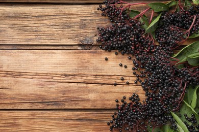 Photo of Elderberries (Sambucus) with green leaves on wooden table, flat lay. Space for text