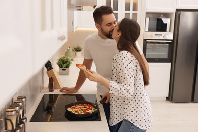 Photo of Happy lovely couple kissing while cooking together in kitchen