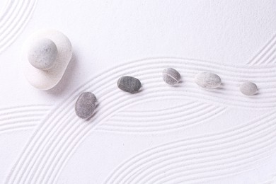 Photo of Zen garden stones on white sand with pattern, flat lay