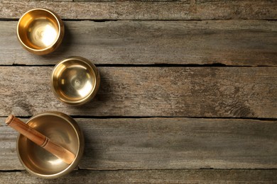 Photo of Golden singing bowls and mallet on wooden table, flat lay. Space for text