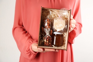 Photo of Woman holding box with stylish craft gift set on light grey background, closeup