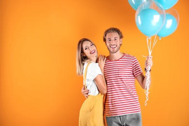 Young couple with air balloons and space for text on color background