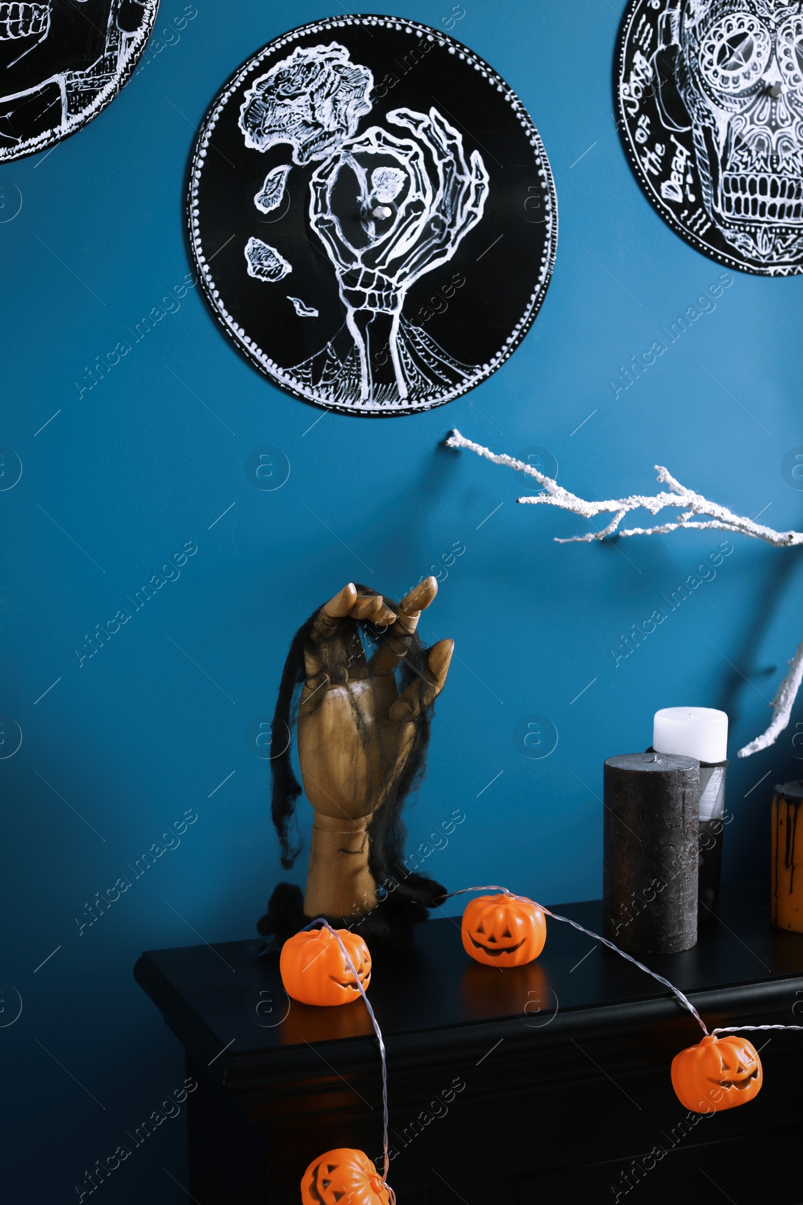 Photo of Jack-o'-lanterns and different Halloween decorations on black fireplace near blue wall