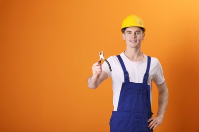 Photo of Young man holding pliers on orange background, space for text