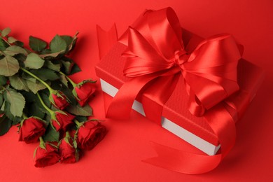 Photo of Beautiful gift box with bow and roses on red background