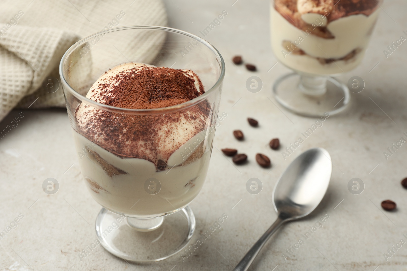 Photo of Delicious tiramisu in glass, spoon and scattered coffee beans on light table