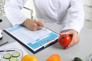 Photo of Scientist with laboratory test form and fresh tomato at table indoors, closeup. Poison detection