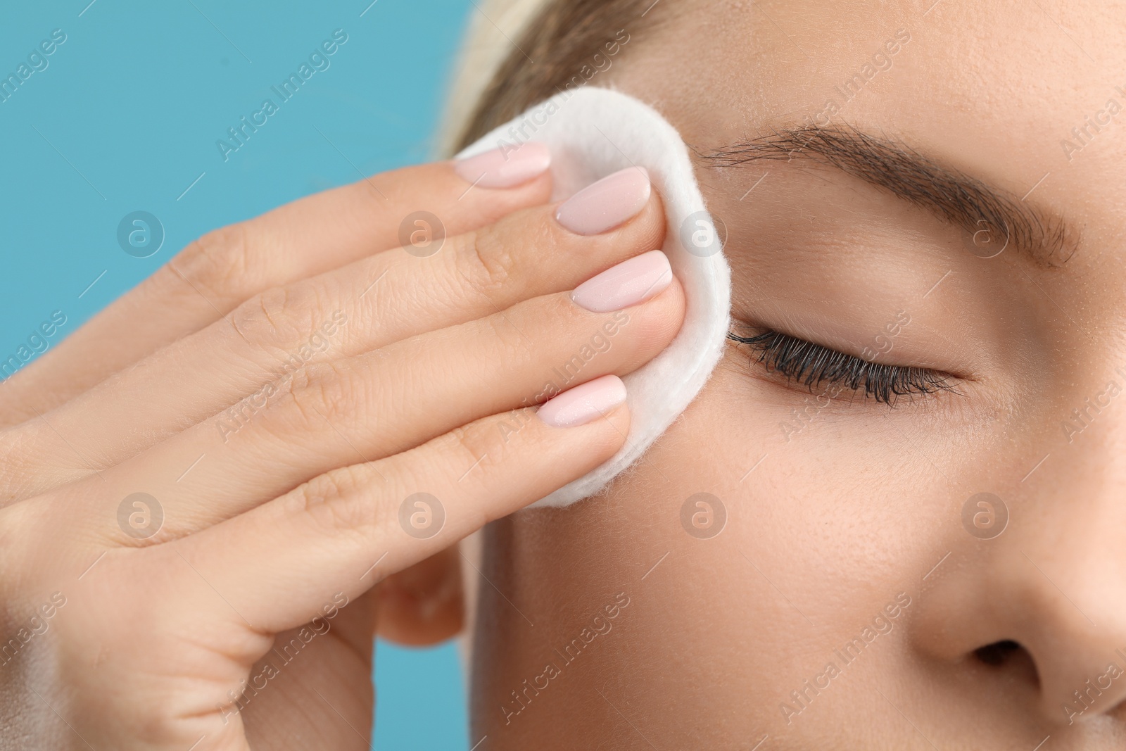 Photo of Woman removing makeup with cotton pad on light blue background, closeup
