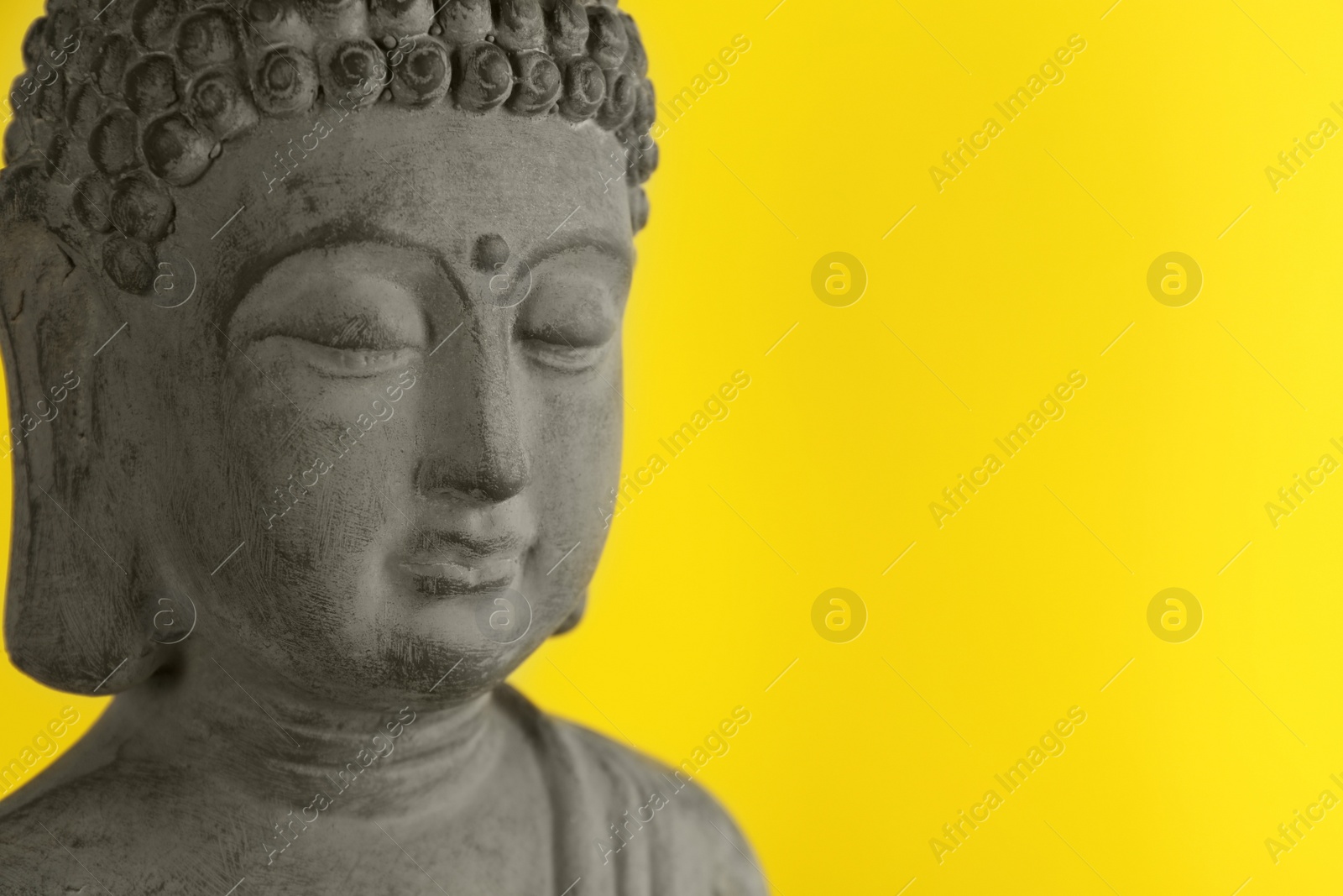 Photo of Beautiful stone Buddha sculpture on yellow background, closeup. Space for text