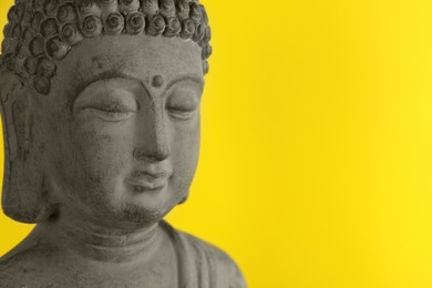 Beautiful stone Buddha sculpture on yellow background, closeup. Space for text