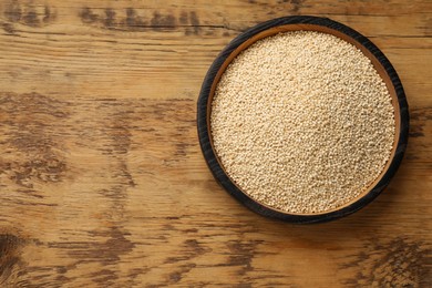 Photo of Dry quinoa seeds in bowl on wooden table, top view. Space for text
