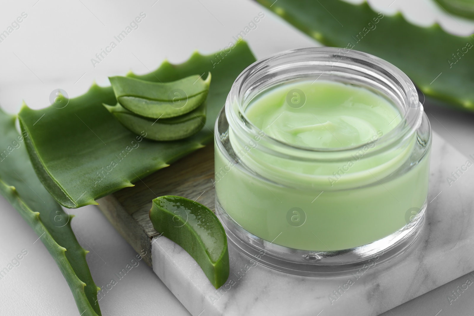 Photo of Jar with cream and cut aloe leaves on white table, closeup